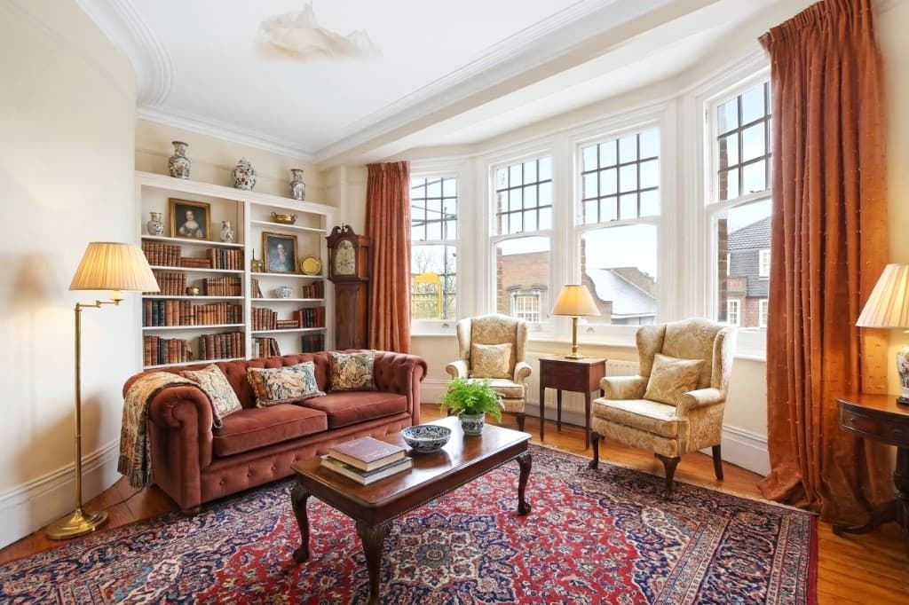The same room virtually staged in a traditional style with Chesterfield sofa, wingback chairs and Persian rug